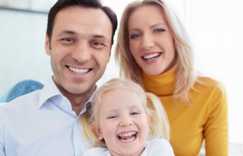 happy family of three : mother, father and a little girl showing beautiful healthy teeth in their smiles