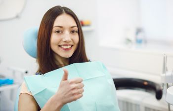 Young woman in a dental chair showing her thumb up after having her teeth checked up Alpharetta GA