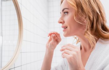 Woman flossing her teeth in front of a mirror.