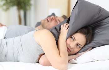 Man snoring while his wife is covering ears with the pillow